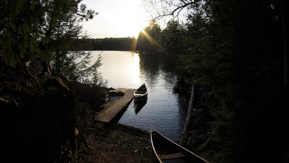 a canoe tied to a dock at the side of a lake